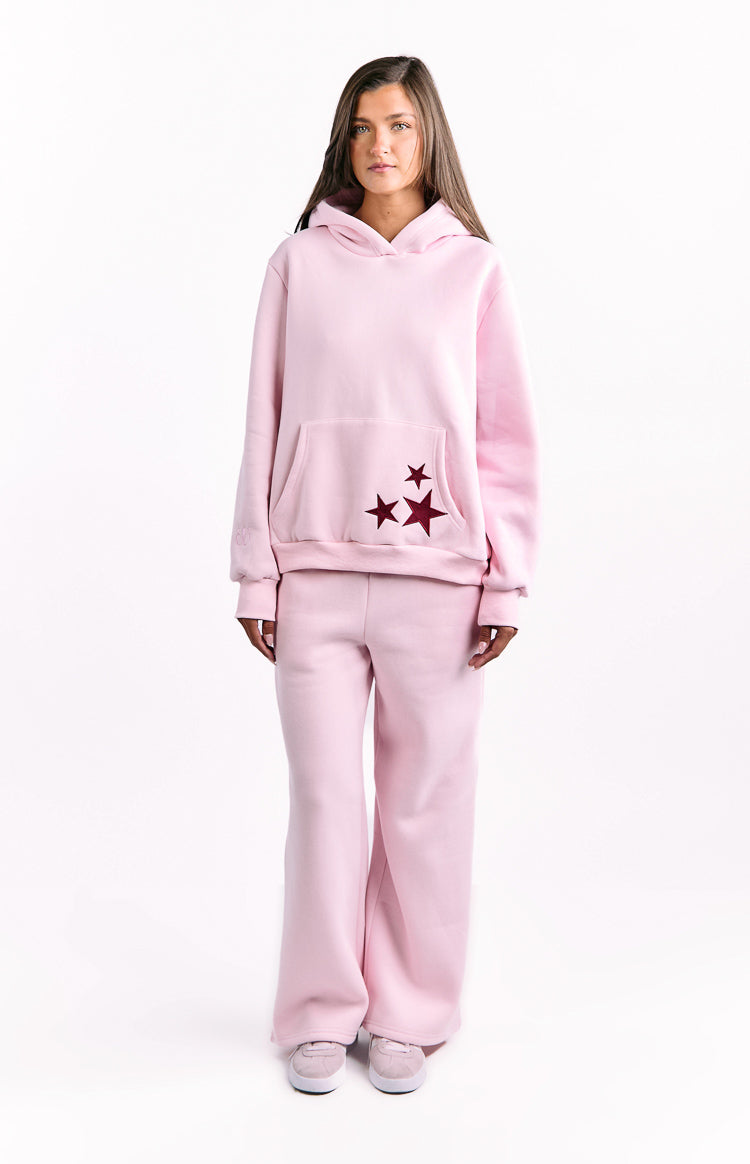Front view of a light pink oversized hoodie featuring a kangaroo pocket with three burgundy stars on the right side
