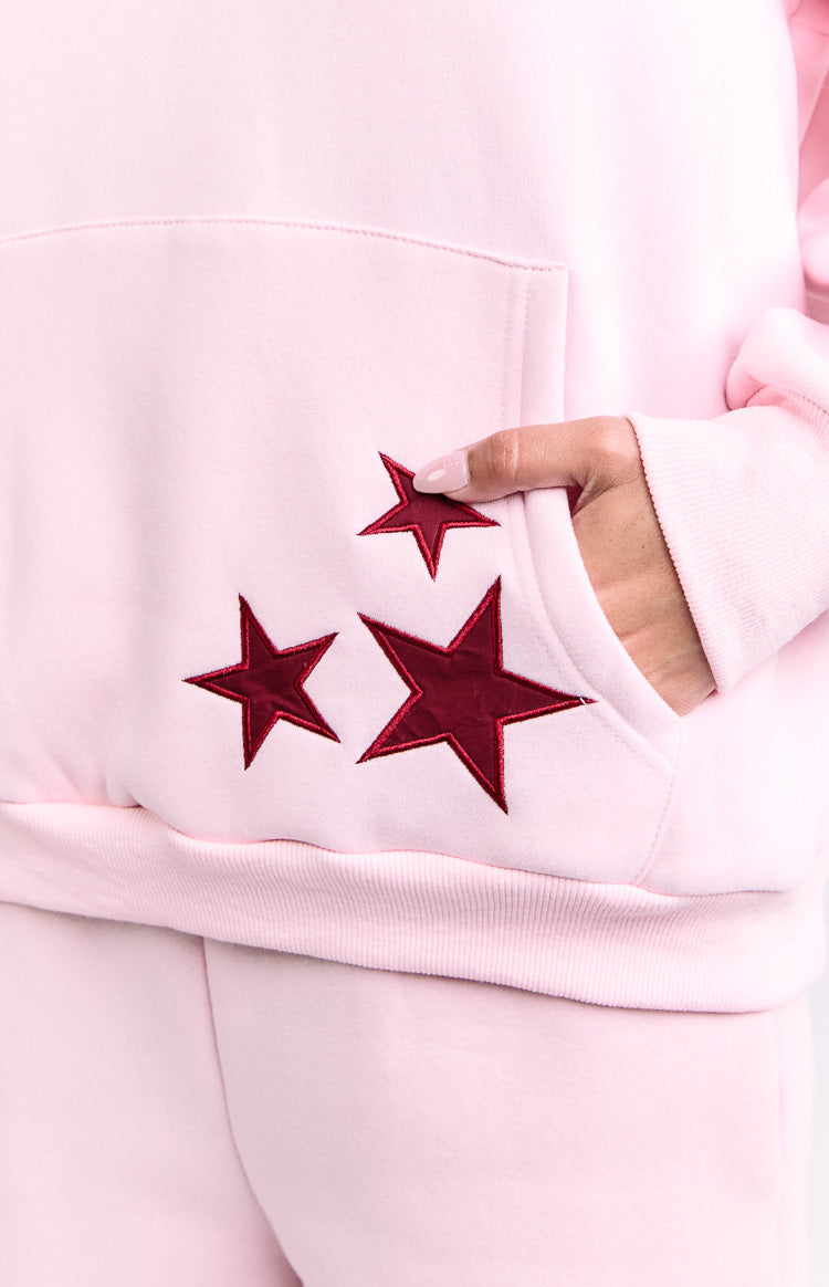 Close-up of the kangaroo pocket on a pink hoodie with three burgundy embroidered stars