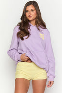 Model in purple tracksuit set, smiling and looking to the side. 