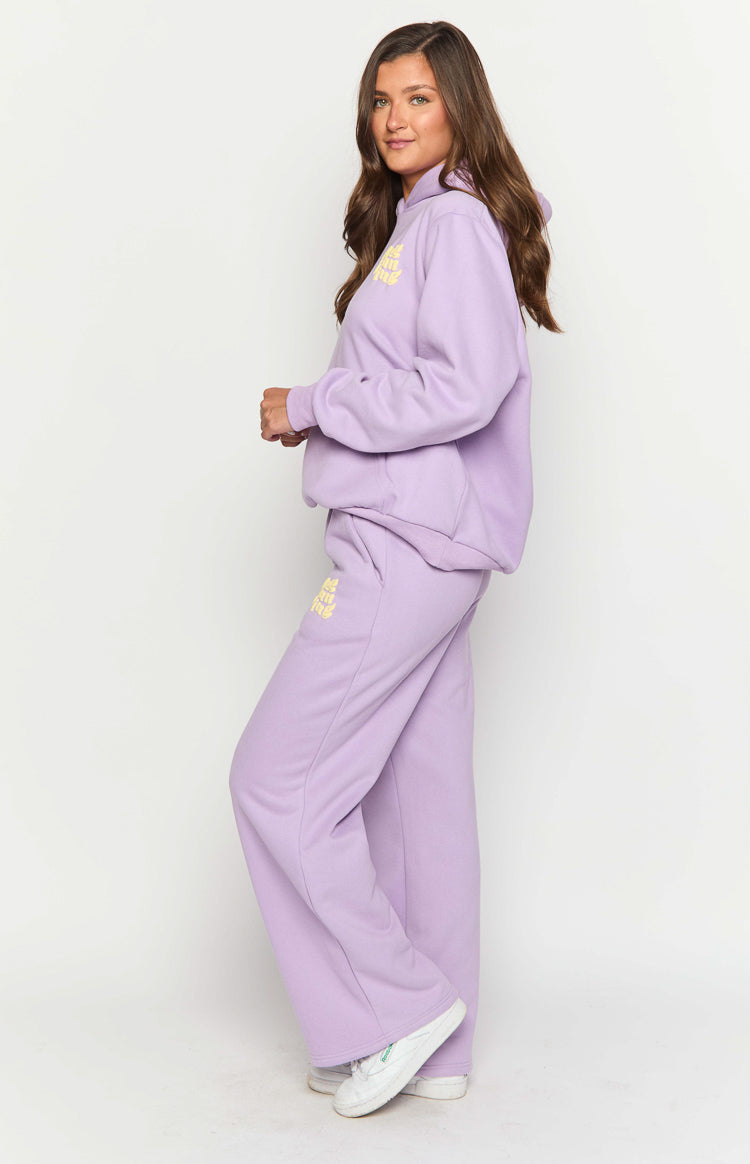 Side view of purple wide-leg track pants with a yellow embroidered logo on the left thigh