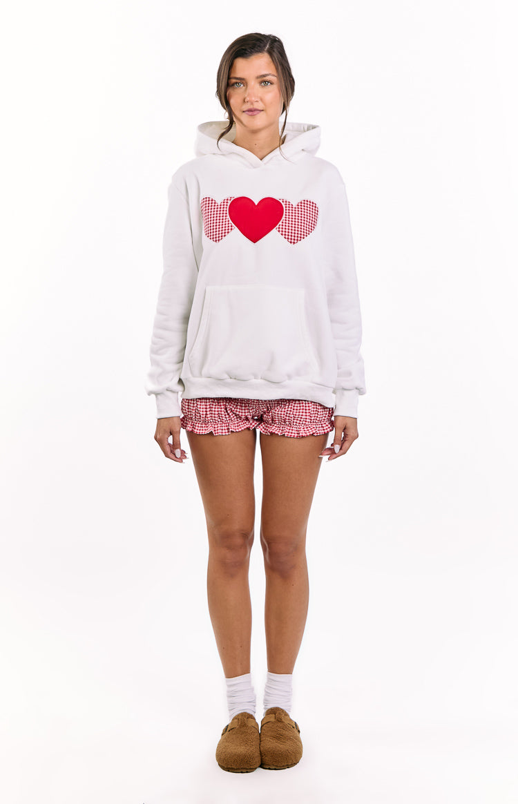 White oversized hoodie with three red heart appliques, two gingham and one solid, and a front kangaroo pocket