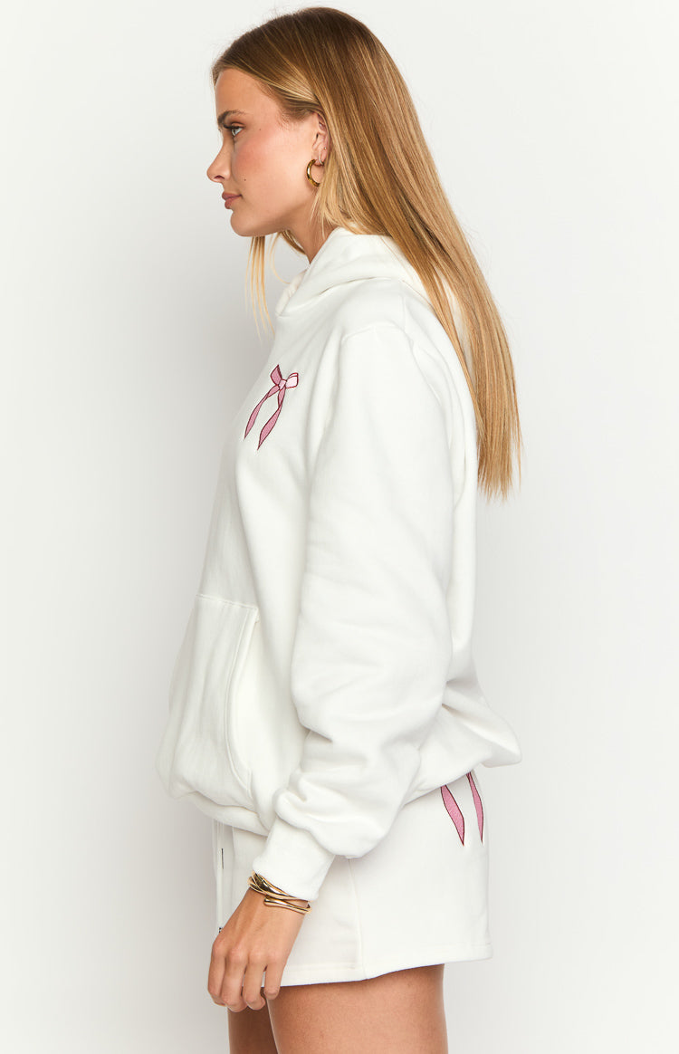 Side view of a white hoodie with a pink bow embroidered on the chest and a front kangaroo pocket