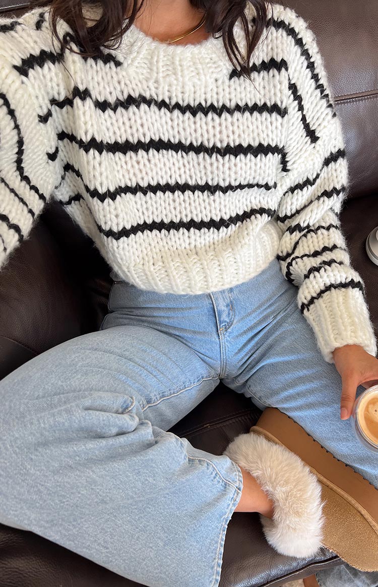 Close-up of a white chunky knit sweater with black stripes, showing the ribbed cuffs and cropped hem