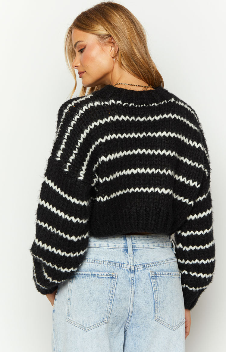 Rear-side view of a black and white striped chunky knit sweater with voluminous sleeves and a cropped hem