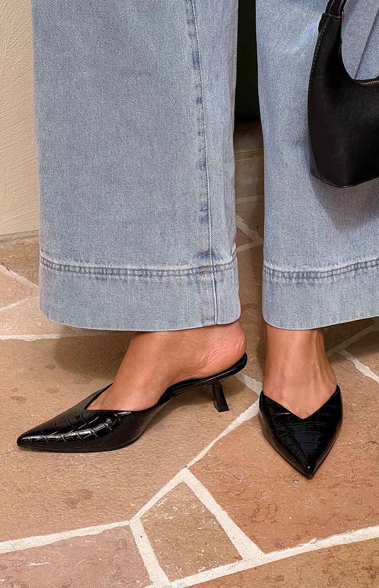 Close-up of black crocodile-embossed pointed-toe mule heels with a V-cut vamp and kitten heel