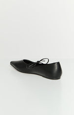 Side-rear view of a black ballet flat with a pointed toe and a tie detail on the vamp