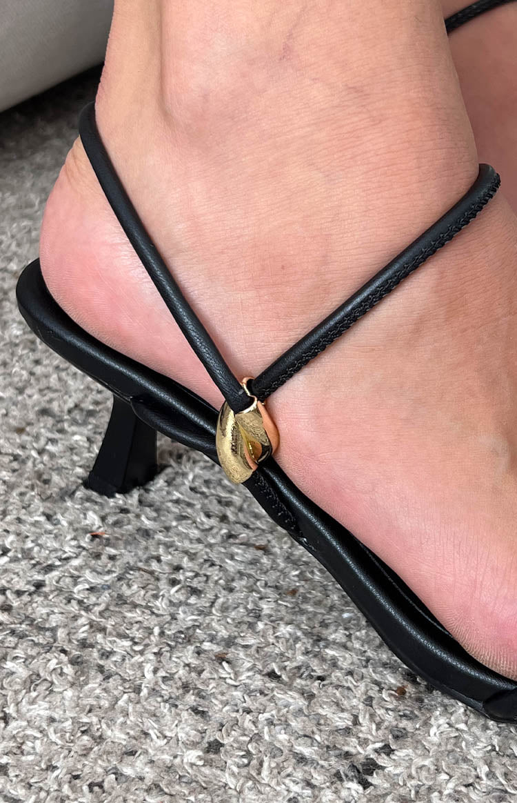 Close-up of the gold hardware detail on the thin black ankle strap of the heels