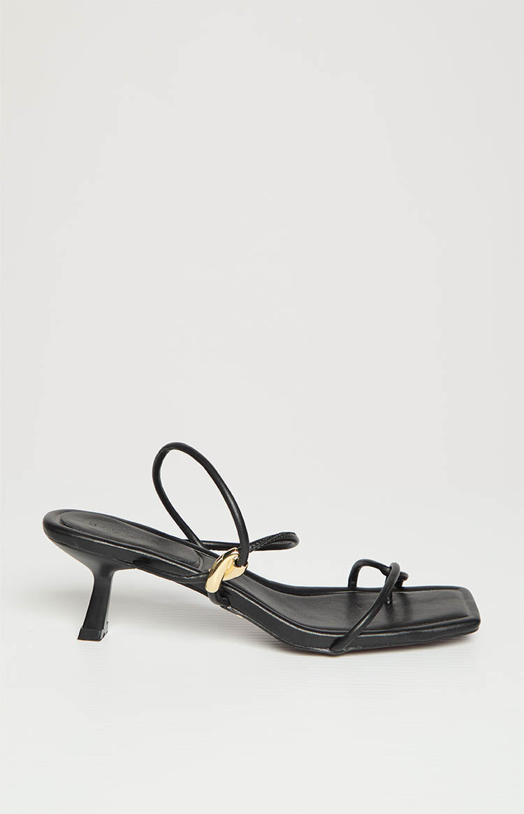 Side profile of black heels featuring a square toe, delicate straps, gold ring detail, and flared kitten heel