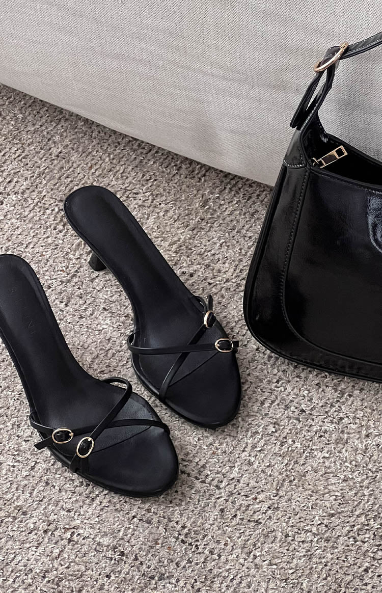 Overhead view of black slip-on heels featuring thin straps with small gold oval buckles