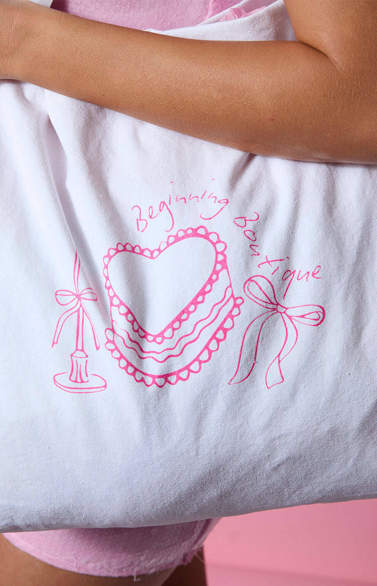 Close-up of the pink graphic print on a white tote bag featuring a heart cake, candle, and bow