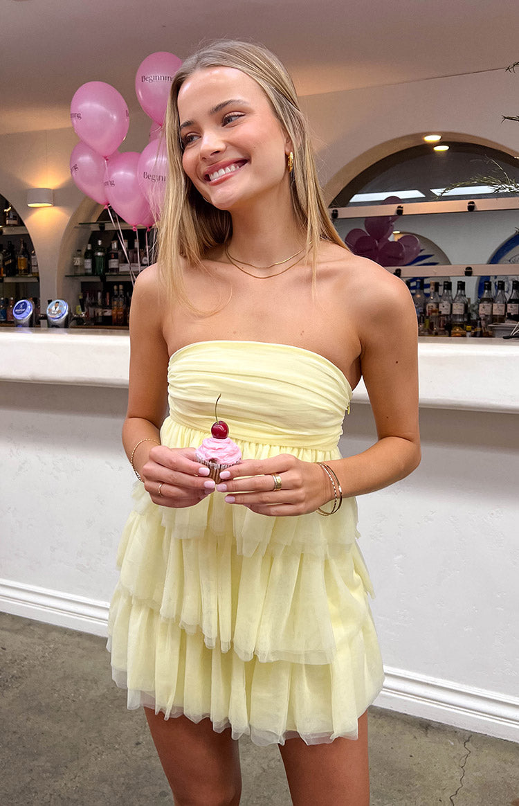 Front view of a yellow strapless mini dress with a ruched bodice and tiered ruffled tulle skirt