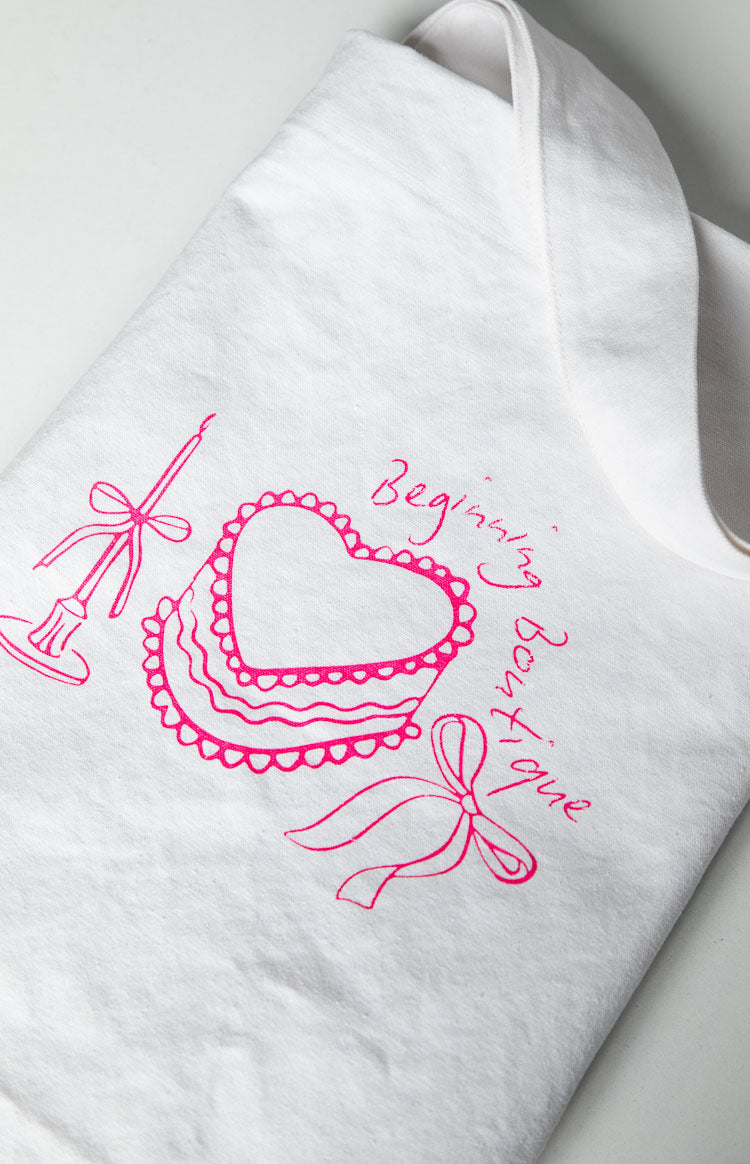 Close-up of the white tote bag's pink graphic print, showing a heart cake, candle, and 'Beginning Boutique' text