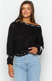 Black chunky knit off-the-shoulder sweater with white lacing detail at the neckline, hem, and sleeve cuffs