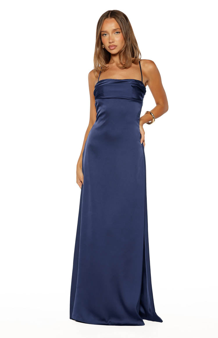 Front view of a navy satin maxi dress with a draped cowl neckline, thin spaghetti straps, and a flowing skirt with a side slit
