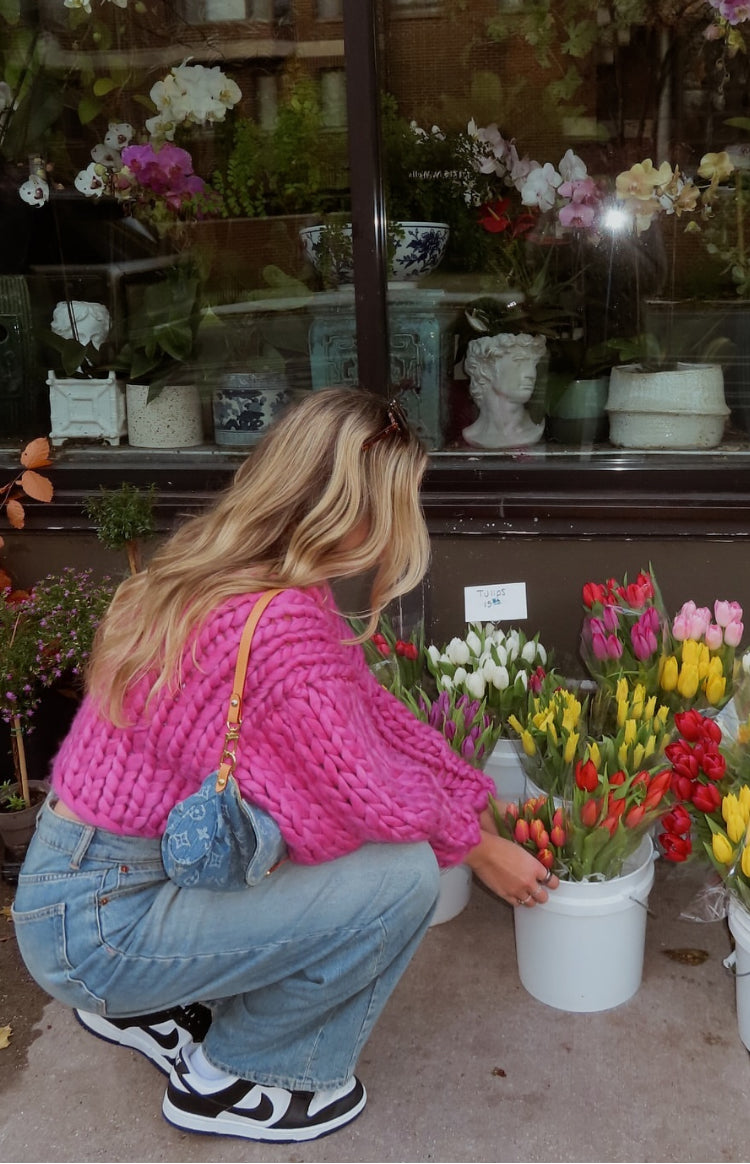 Rear-side view of a bright pink chunky knit cardigan with a cropped hem and voluminous sleeves