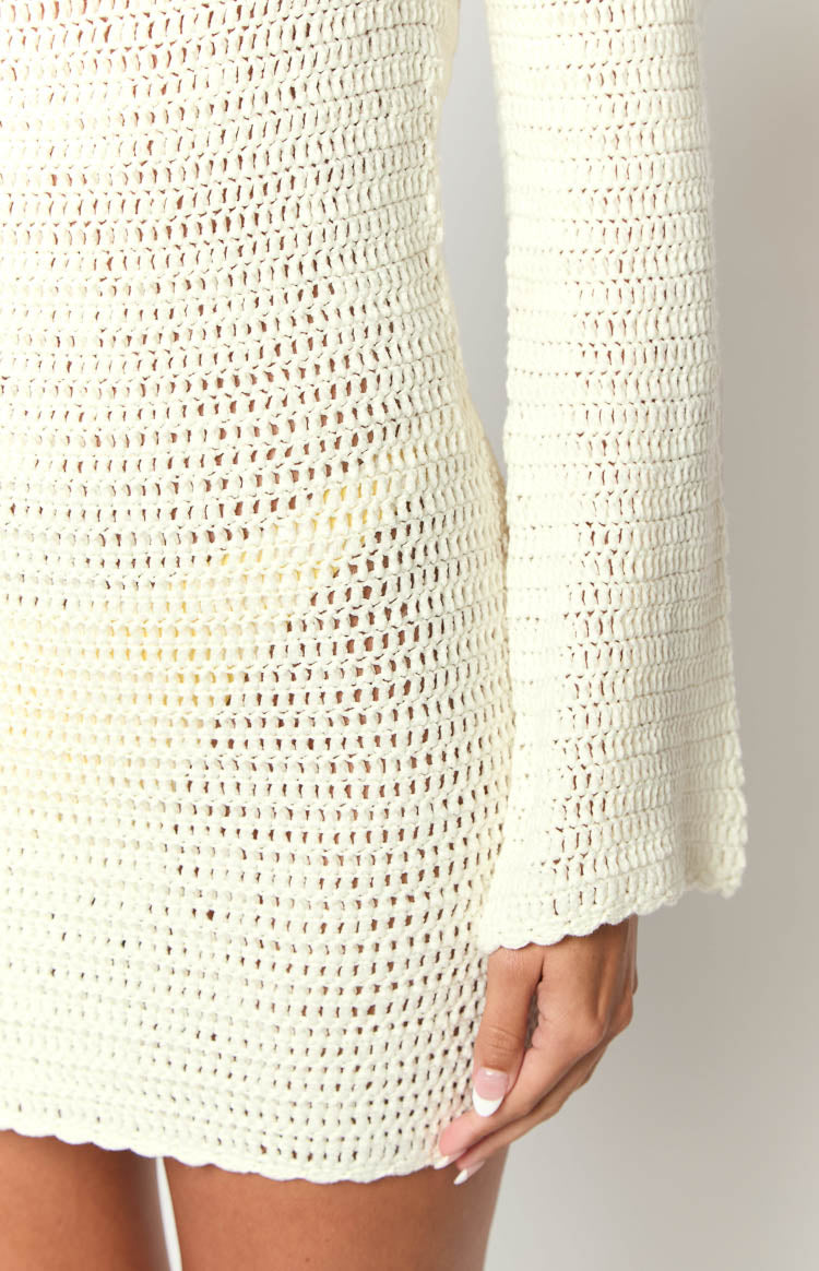 Close-up of the white open crochet knit mini dress, highlighting the fabric texture and long flared sleeve