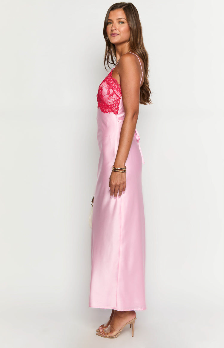 Side view of a pink satin maxi dress featuring a red lace bust, thin spaghetti straps, and a tie detail at the back waist