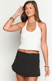 Front view of a black mini skirt with white polka dots, featuring a ruched waistband and a flared hem