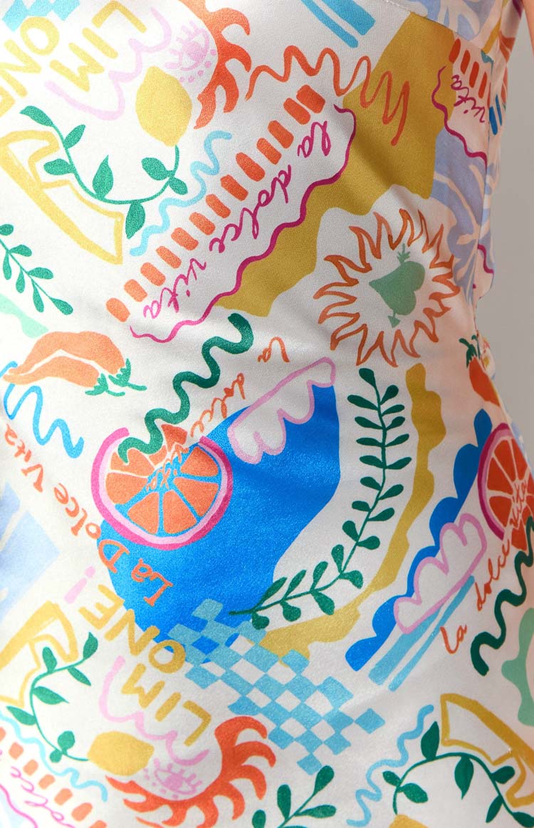 Close-up of the white maxi dress fabric with a colourful La dolce vita print featuring lemons, oranges, chili peppers, and wavy lines