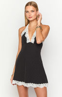 Blonde model wearing a black polka dot mini dress with a halter neckline and contrast white lace trim
