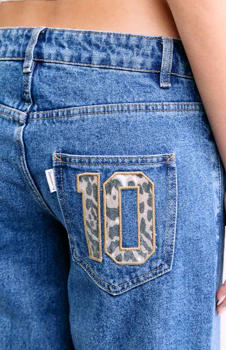 Close-up of the back pocket on mid-wash denim jeans with a large leopard print '10' applique