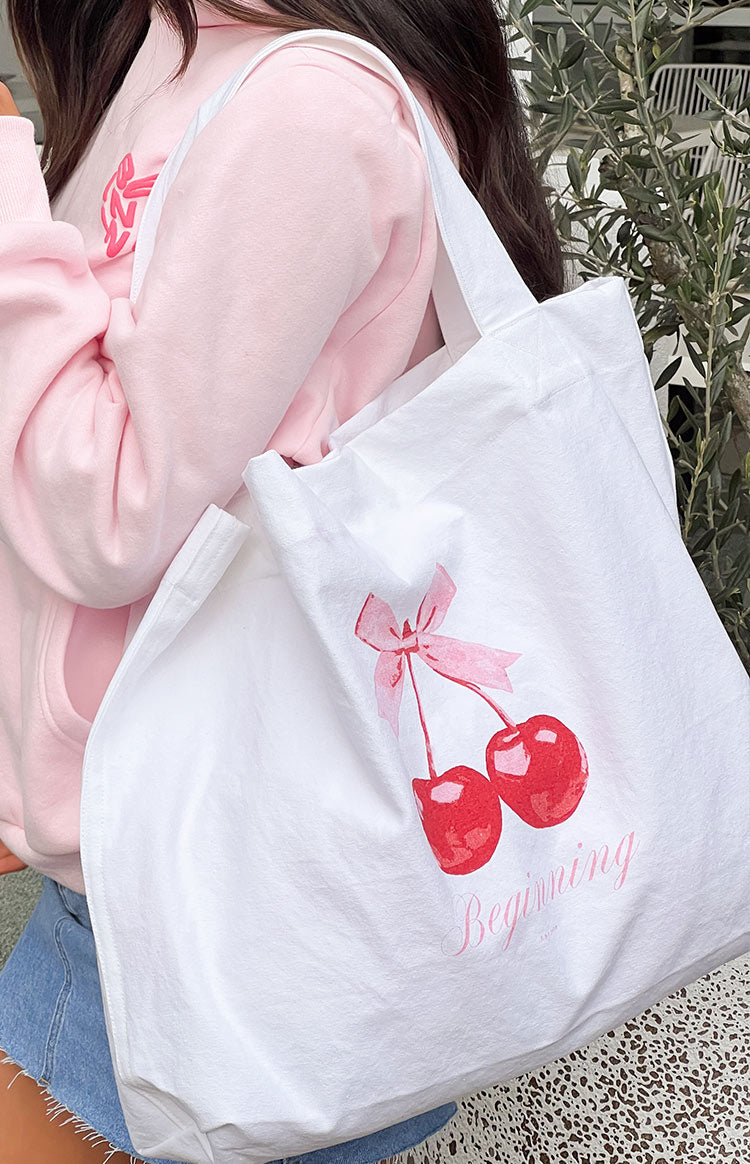 Close-up of the white tote bag featuring a red cherry graphic with pink bow and 'Beginning' text