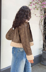 Side view of a distressed brown aviator jacket with cream sherpa lining at the cropped hem and cuffs