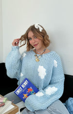 Close-up of a light blue chunky knit sweater with white cloud appliques and oversized balloon sleeves