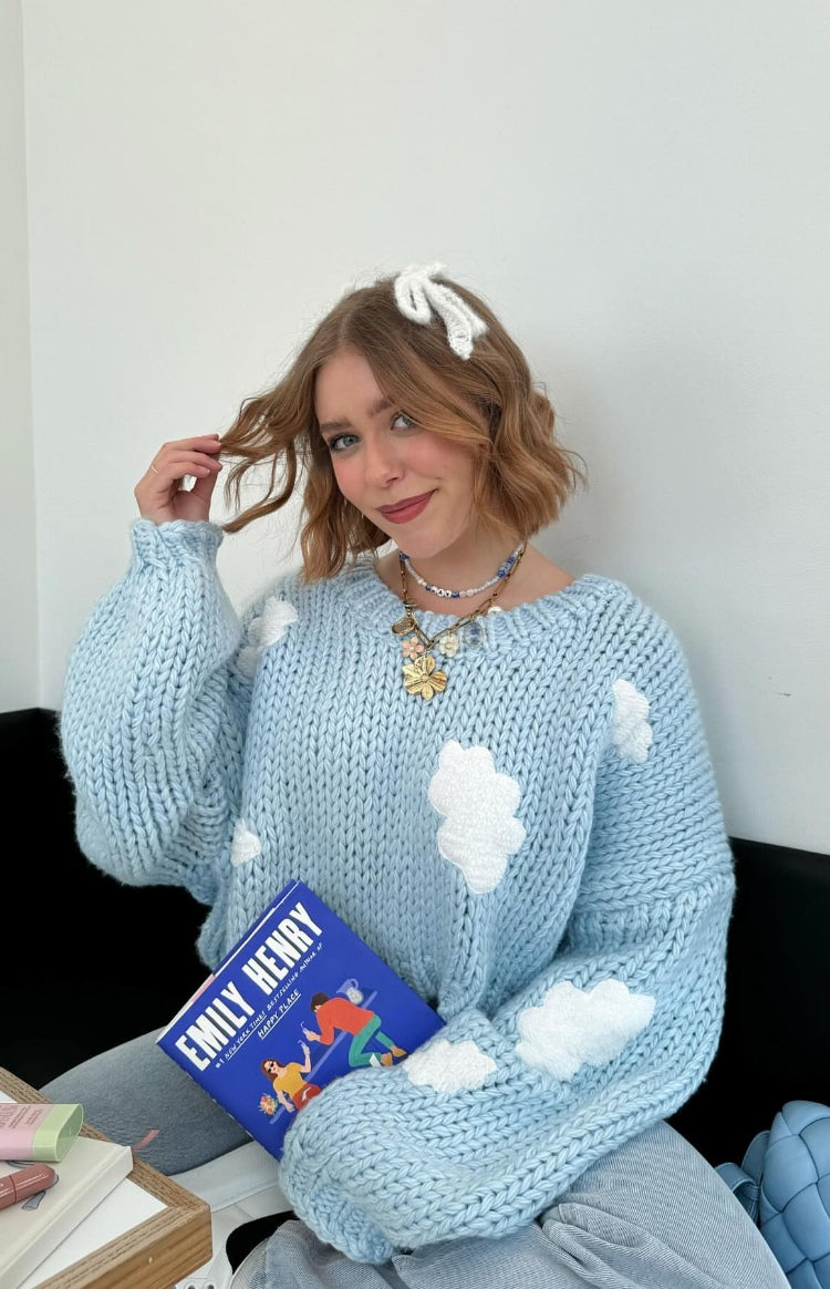 Close-up of a light blue chunky knit sweater with white cloud appliques and oversized balloon sleeves