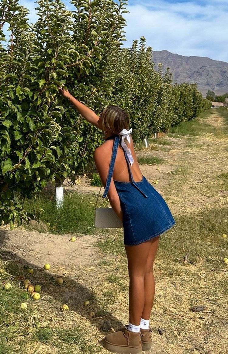 Rear view of a dark wash denim mini dress with an open back and thick halter straps