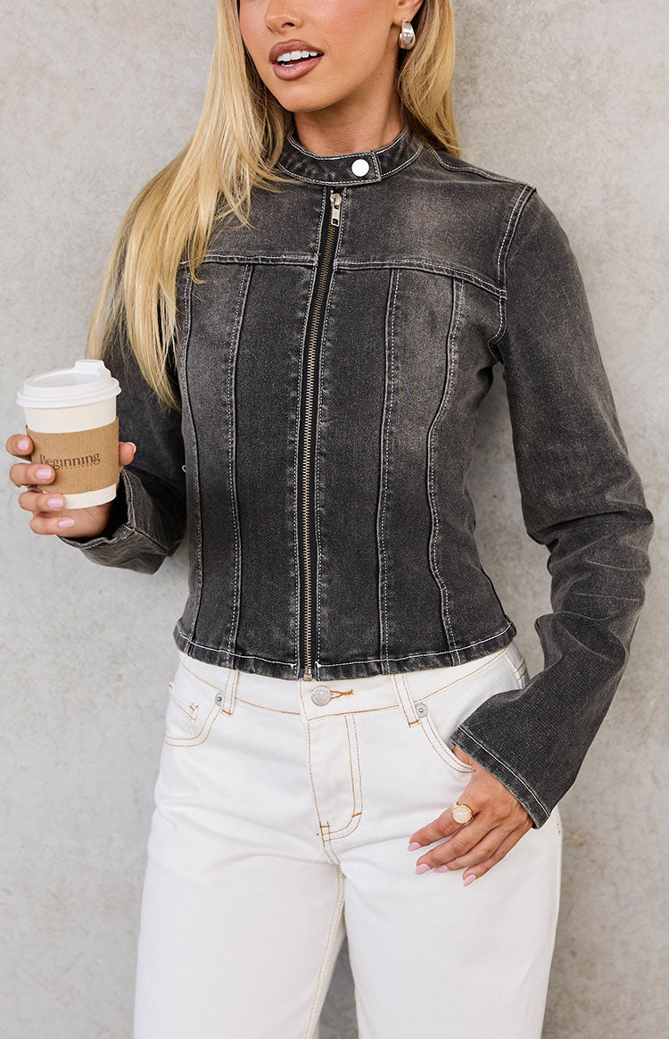 Close-up front view of a washed black denim biker jacket with a stand collar, vertical seam detailing, and white contrast stitching