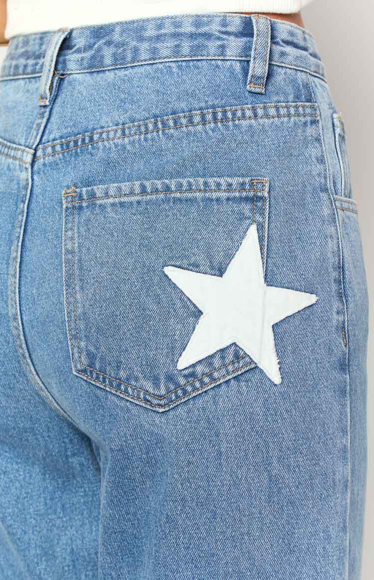 Close-up of the back pocket on mid-wash denim jeans with a large white star patch