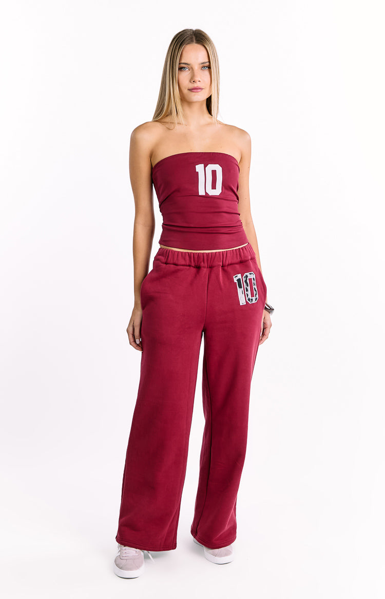 Full length view of burgundy wide-leg track pants with an elasticated waist and a white leopard print '10' patch on the left thigh