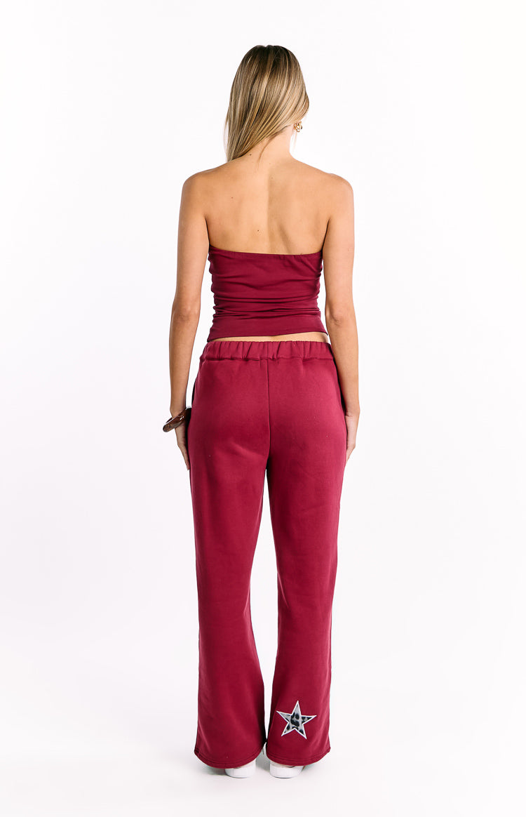 Rear view of burgundy track pants with an elasticated waist and a leopard print star on the lower left leg