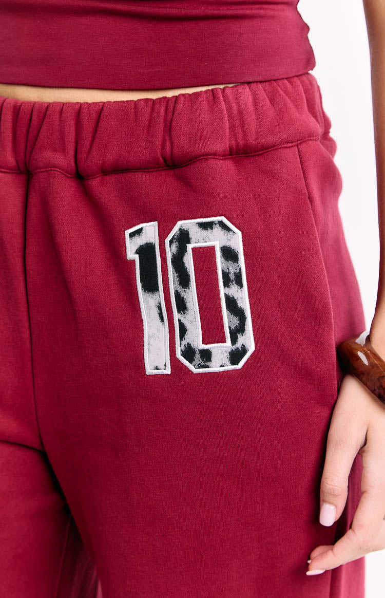 Close-up of the elasticated waistband and the white outlined leopard print '10' on burgundy track pants