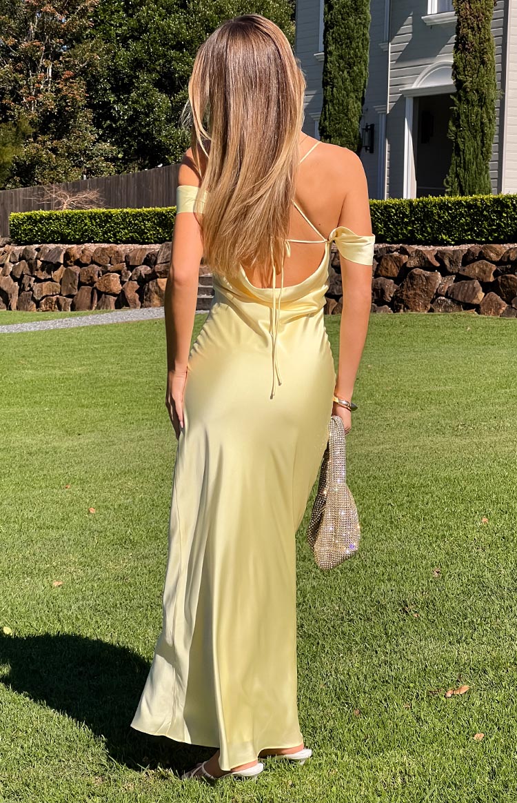 Back view of a pale yellow satin formal maxi dress- featuring elegant off-the-shoulder sleeves and a detailed criss-cross tie-back- creating a sophisticated silhouette for a formal event or prom.