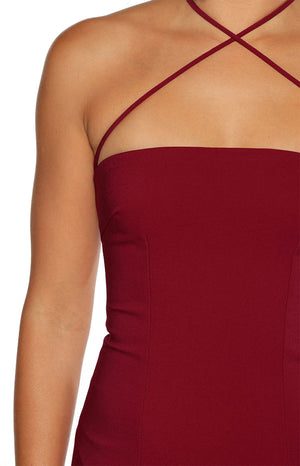 A close-up of our model wearing a burgundy maxi dress features a straight strapless bodice with subtle vertical seam detailing. The thin matching fabric spaghetti straps emerge from the top edge and crisscross over the chest to form a halter neckline.