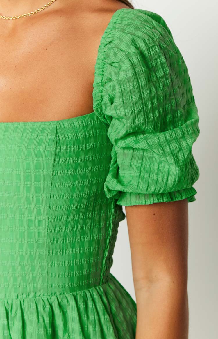 Close-up of the green playsuit showing the textured checked fabric and short puffed sleeve with elasticated cuff