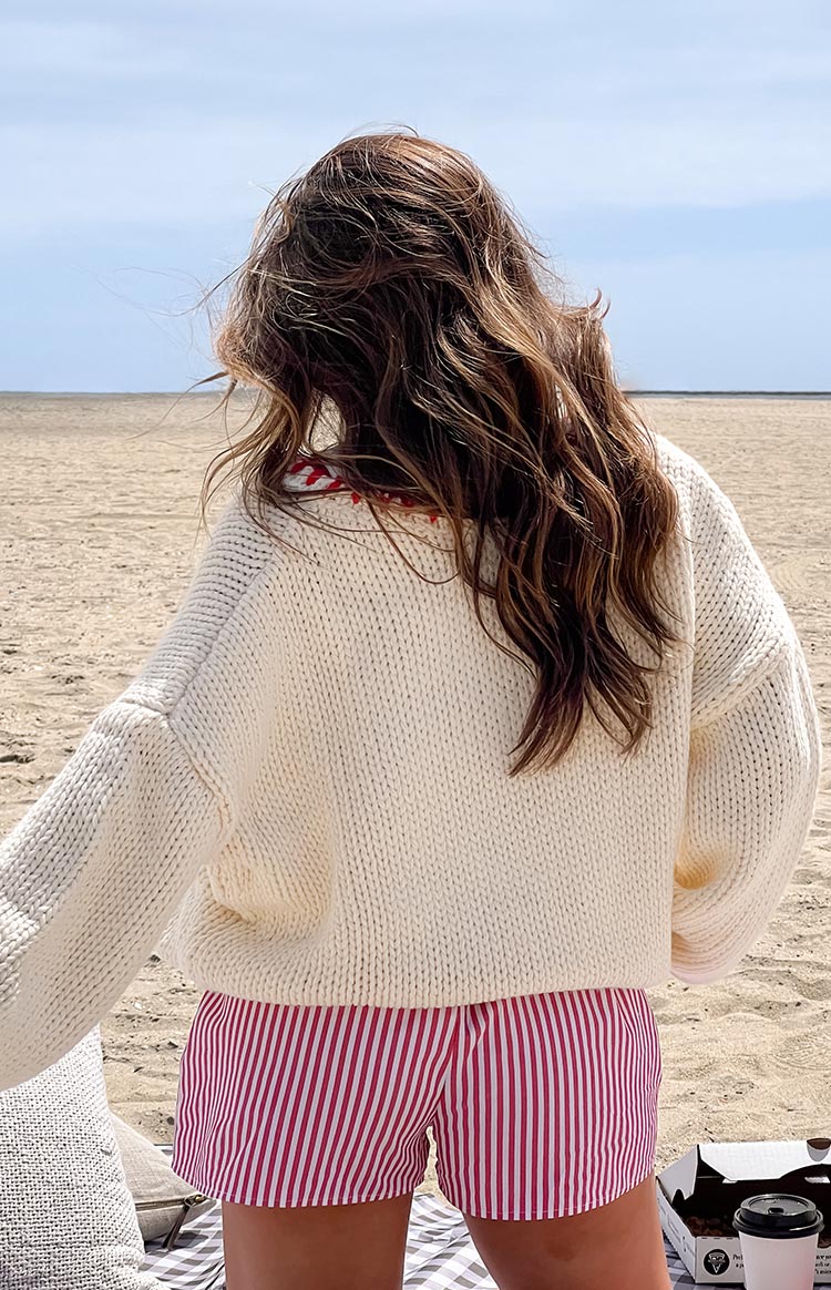 Rear view of a cream chunky knit sweater with red contrast stitching around the back of the neck and dropped shoulders