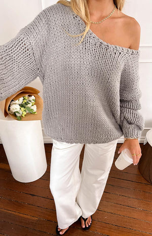 blonde girl wearing an oversized asymmetric light grey knit sweater paired with white jeans