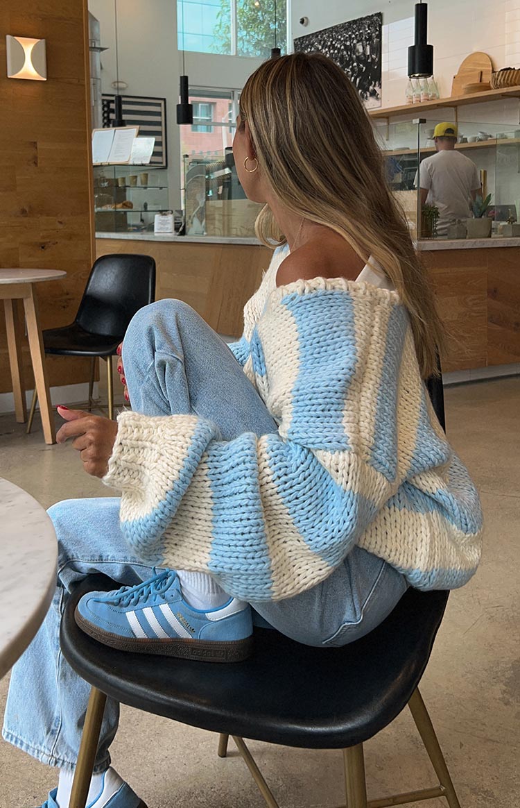 Side view of an oversized light blue and cream striped chunky knit sweater with wide sleeves and an off-shoulder neckline