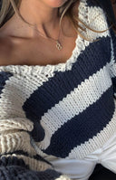 Off-the-shoulder neckline of a navy and cream striped chunky knit sweater with a relaxed fit