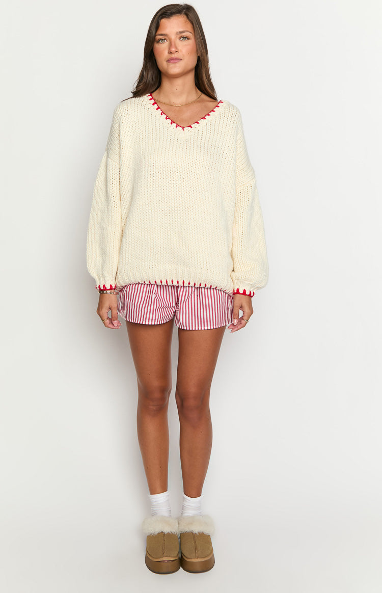 Cream chunky knit sweater with an oversized fit, V-neck, and red contrast stitching on neckline, cuffs, and hem