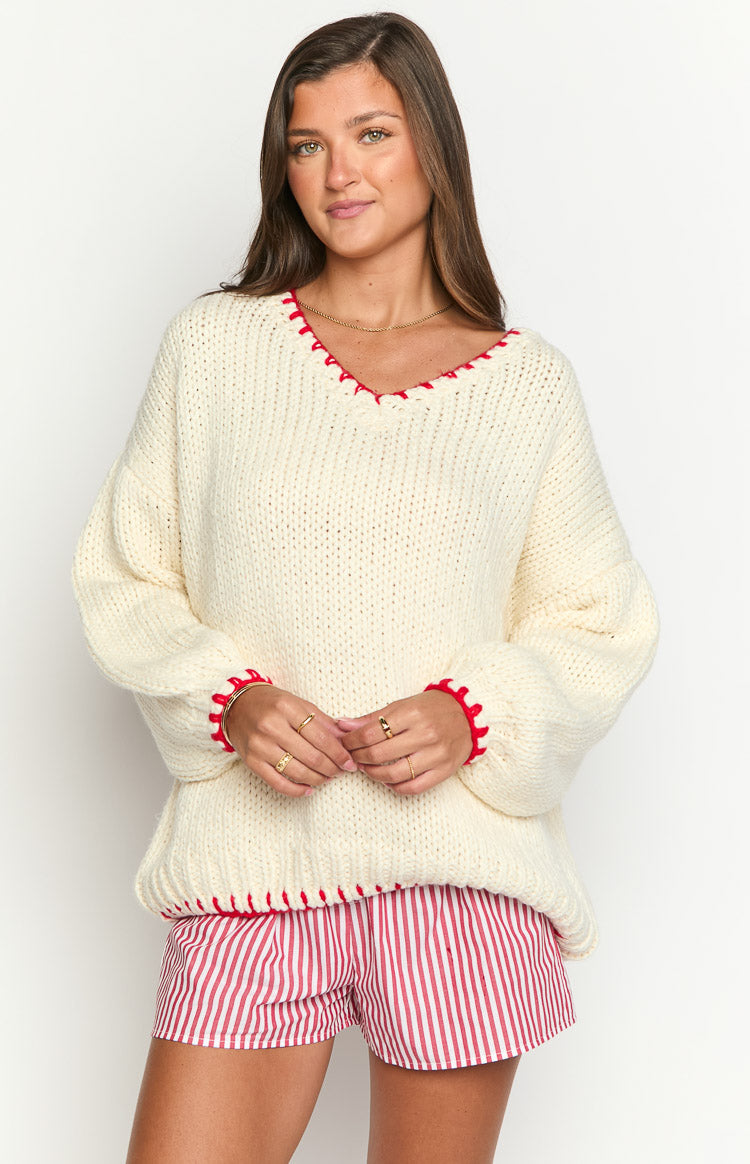 Front view of an oversized cream chunky knit sweater with red contrast stitching on the V-neckline, cuffs, and hem