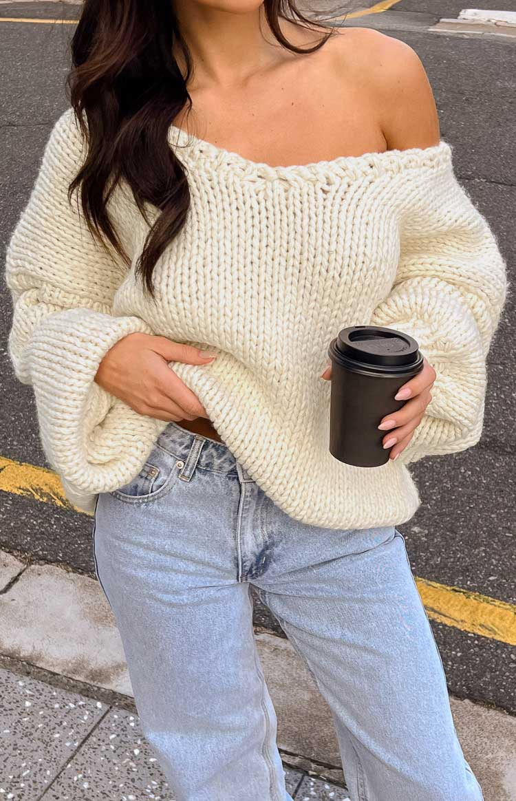 Close-up of the cream chunky knit sweater showing the wide off-shoulder V-neckline and oversized cuffed sleeves