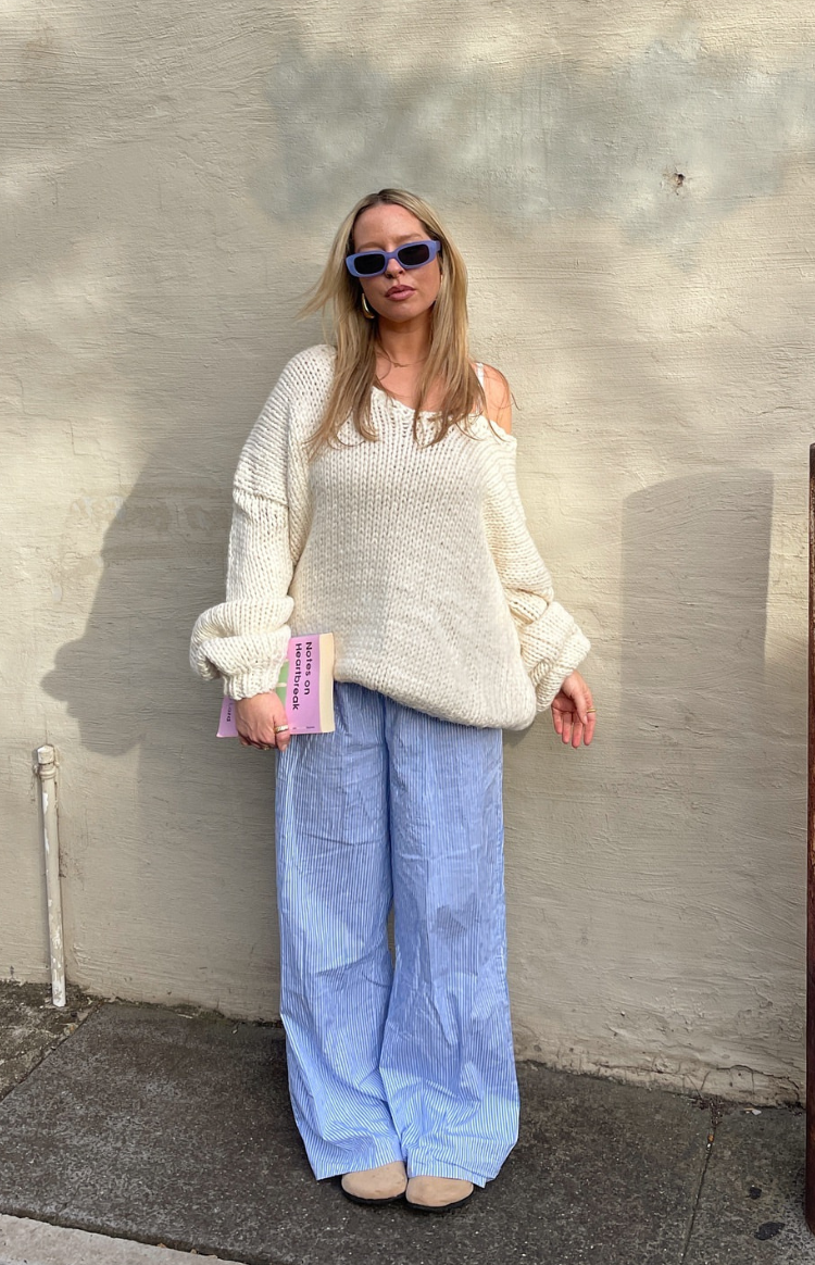 Cream chunky knit sweater with an oversized fit, V-neck, and long voluminous sleeves worn off one shoulder