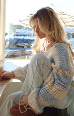 Side view of a light blue and cream striped chunky knit sweater with oversized sleeves