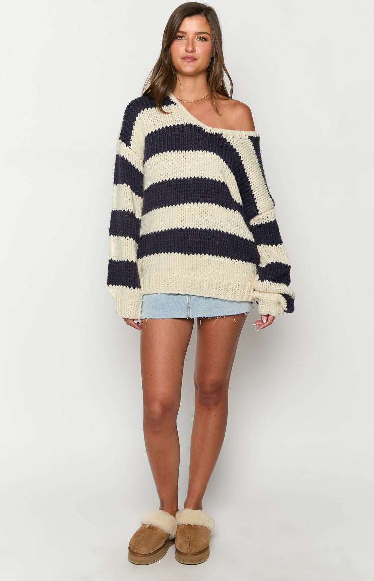 Full length view of the oversized navy and cream striped chunky knit sweater with a wide V-neck worn off one shoulder