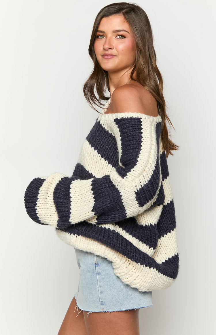Side view of a navy and cream striped chunky knit sweater with an off-shoulder neckline and voluminous sleeves