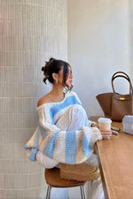 Light blue and white striped chunky knit sweater with a wide off-shoulder neckline and oversized sleeves